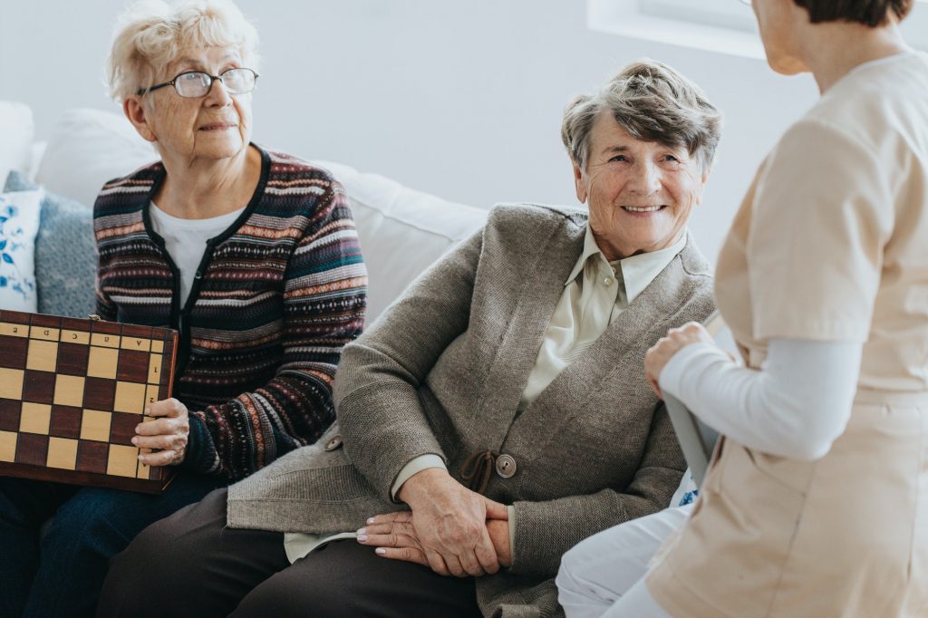 Older ladies sit on a couch and talk to a nurse at a local nursing home